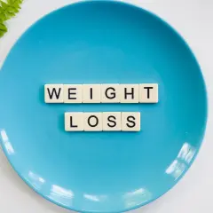Niebieski talerz z literami "WEIGHT LOSS" i gałązką paproci. Czy to znak, że za mało kalorii na redukcji?