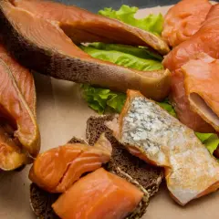 Kawałki wędzonego łososia na liściach sałaty i ciemnym pieczywie. Czy łosoś wędzony jest zdrowy? Tak, to bogactwo kwasów omega-3.