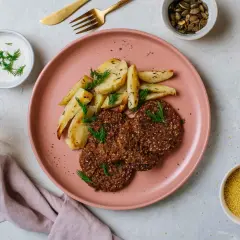 Na talerzu pieczone ziemniaki i kotleciki z kaszy, obok miseczka z jogurtem i koprem. To idealna zdrowa kolacja.