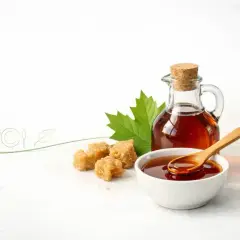 Syrop klonowy w butelce i miseczce, obok kostki cukru i liścia klonu. Czy syrop klonowy jest zdrowy?