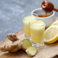 Dwa kieliszki z żółtym płynem, obok świeży imbir, plasterki cytryny i miód. Idealny syrop z tymianku i imbiru na przeziębienie.