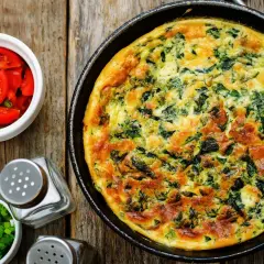 Frittata ze szpinakiem i serem, idealna jako pomysł, czym zastąpić węglowodany. Obok pomidorki i szczypiorek.