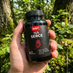 Dłoń trzyma czarny suplement na serce "Na Serce" z czerwonym logo i grafiką serca. Tło to las.