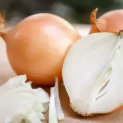 Cała i przekrojona cebula, obok pokrojone plastry cebuli na drewnianym tle.