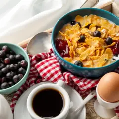 Pyszne węglowodany na śniadanie: płatki kukurydziane z jagodami i dżemem, jajko na miękko, muffin i kawa.