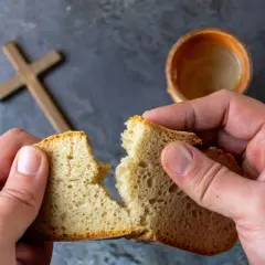 Dłonie łamią chleb, symbolizując post ścisły. W tle krzyż i kielich.