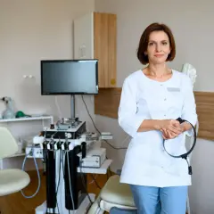 Lekarka w gabinecie foniatrycznym, z aparaturą medyczną w tle. Czy badanie u foniatry jest bolesne? Niekoniecznie, nowoczesny sprzęt i doświadczenie lekarza minimalizują dyskomfort.
