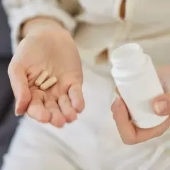 Dwie kapsułki na dłoni i biały pojemnik. Zastanawiasz się, colostrum na co? To naturalne wsparcie dla odporności.
