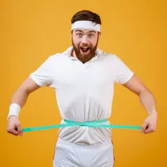 Zaskoczony mężczyzna w stroju sportowym mierzy talię. Zastanawia się, ile można przytyć w tydzień.