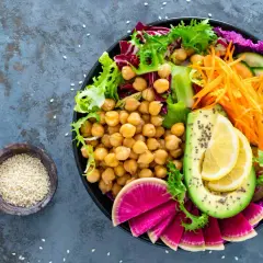 Kolorowa buddha bowl z ciecierzycą, awokado, rzodkiewką, ogórkiem, marchewką i sałatą.