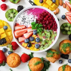 Kolorowa miska smoothie z owocami: truskawki, kiwi, mango, jagody, maliny, jeżyny, granat. Obok muffinki i migdały. Zdrowe produkty, które mogą zawierać histaminę.