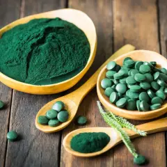 Chlorella vs spirulina: zielony proszek i tabletki na drewnianym tle. Dwa rodzaje alg w formie suplementów diety.