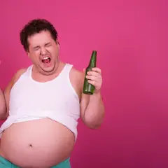 Mężczyzna z piwnym brzuchem krzyczy, trzymając kufel piwa i butelkę, zastanawiając się, czy wódka tuczy.