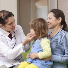 Lekarka bada dziecko, które może mieć niedoczynność tarczycy. Obok siedzi matka.