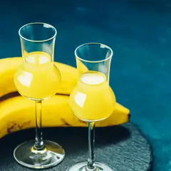 Dwa kieliszki z żółtym płynem, obok kiść bananów. To idealny moment na domową nalewkę z banana.