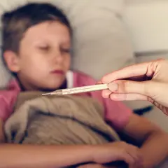 Dziecko 10 lat leży chore, ma zimne ręce. Mama mierzy mu temperaturę.