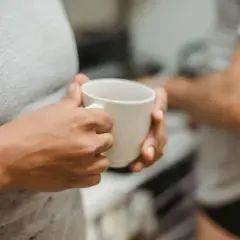 Dłonie trzymają biały kubek, symbolizując chwilę spokoju i początek detoksu od kawy.