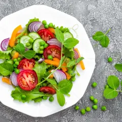 Kolorowa sałatka z pomidorów, ogórków, marchewki, cebuli i groszku na talerzu. Idealna na zdrową dietę warzywną.