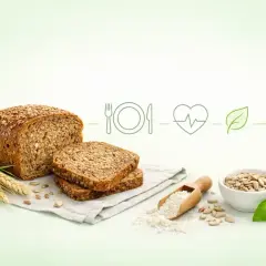 Pełnoziarniste pieczywo na diecie to zdrowy wybór. Na zdjęciu bochenek chleba, kromki, nasiona słonecznika, mąka i kłosy zboża.