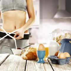 Kobieta mierzy talię, obok zdrowe śniadanie: jajka, płatki, mleko, sok. Idealny jadłospis na dieta 1 kg tygodniowo.