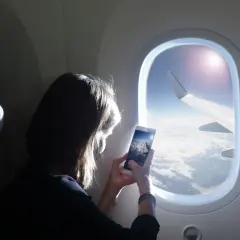 Kobieta robi zdjęcie z telefonu widoku z okna samolotu. Widok na chmury i skrzydło samolotu. Idealny moment dla tych, którzy nie boją się wysokości i chcą uwiecznić podróż.