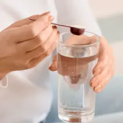 Kobieta dodaje miarkę kolagenu końskiego dla ludzi do szklanki wody.