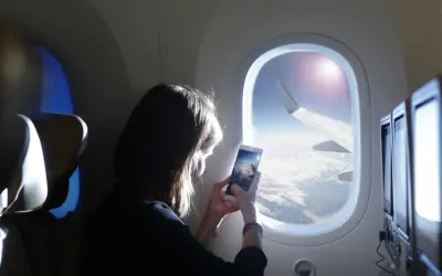 Kobieta robi zdjęcie z telefonu widoku z okna samolotu. Widok na chmury i skrzydło samolotu. Idealny moment dla tych, którzy nie boją się wysokości i chcą uwiecznić podróż.