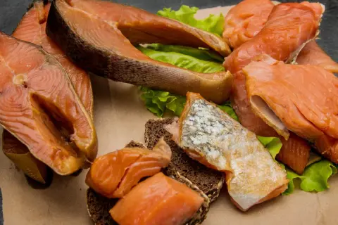 Kawałki wędzonego łososia na liściach sałaty i ciemnym pieczywie. Czy łosoś wędzony jest zdrowy? Tak, to bogactwo kwasów omega-3.