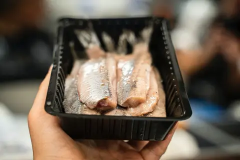 Dłoń trzyma opakowanie ze śledziami. Czy śledź jest zdrowy? Tak, to bogate źródło kwasów omega-3.