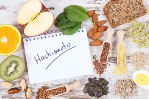 Zdrowe produkty i notatnik z napisem "Hashimoto". Rozważ jakie suplementy przy niedoczynności tarczycy mogą pomóc.