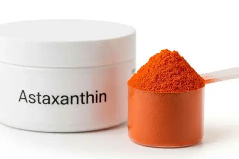 Słoiczek z napisem "Astaxanthin" i miarka pełna pomarańczowego proszku. Poznaj astaksantyna działanie!