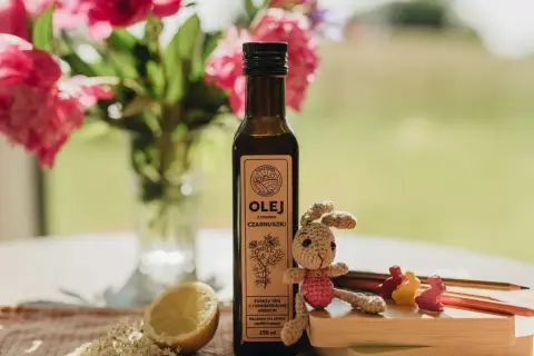 Olej z czarnuszki w butelce, obok cytryny, kwiatów i szydełkowego zajączka. Od jakiego wieku można go stosować?
