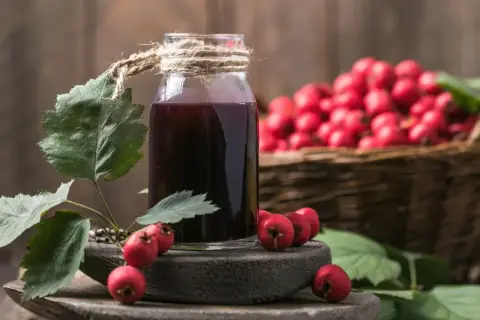 Butelka z nalewką z głogu na serce, obok gałązka z owocami i kosz pełen głogu.