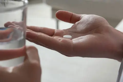 Dłoń z tabletką maślanu sodu i szklanka wody, przygotowanie do połknięcia leku w ciąży.