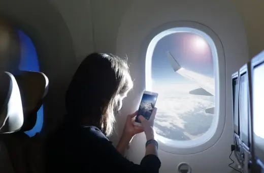 Kobieta robi zdjęcie z telefonu widoku z okna samolotu. Widok na chmury i skrzydło samolotu. Idealny moment dla tych, którzy nie boją się wysokości i chcą uwiecznić podróż.