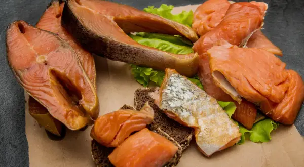 Kawałki wędzonego łososia na liściach sałaty i ciemnym pieczywie. Czy łosoś wędzony jest zdrowy? Tak, to bogactwo kwasów omega-3.