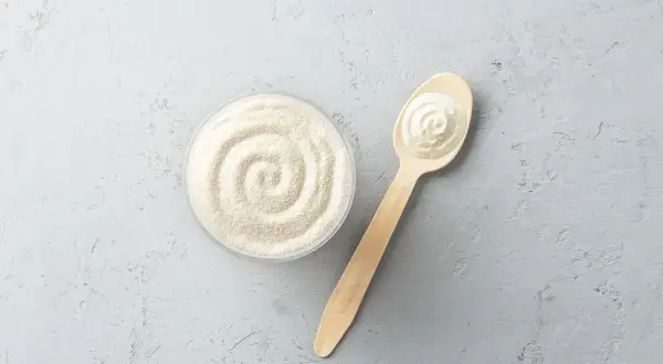 Sypkie peptydy na stawy w miseczce i na drewnianej łyżce, gotowe do użycia dla zdrowia.