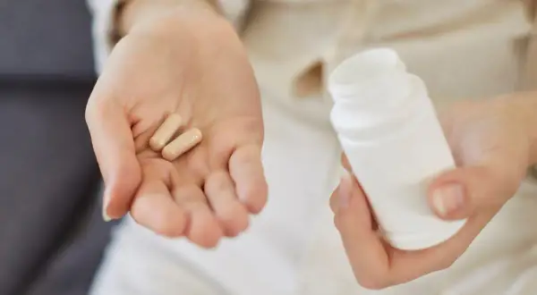 Dwie kapsułki na dłoni i biały pojemnik. Zastanawiasz się, colostrum na co? To naturalne wsparcie dla odporności.