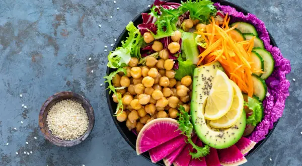 Kolorowa buddha bowl z ciecierzycą, awokado, rzodkiewką, ogórkiem, marchewką i sałatą.