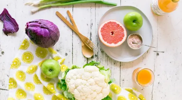 Jabłka i grejpfruty to owoce, które pomagają obniżyć cholesterol. Na zdjęciu widzimy też kalafior, czerwoną kapustę i szczypiorek.