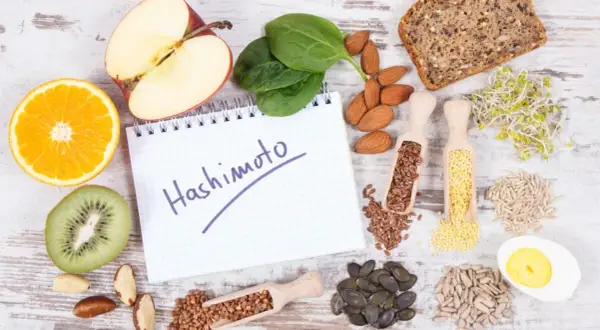 Zdrowe produkty i notatnik z napisem "Hashimoto". Rozważ jakie suplementy przy niedoczynności tarczycy mogą pomóc.