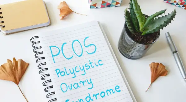Notatnik z napisem "PCOS Polycystic Ovary Syndrome" obok sukulentów i ozdobnych pudełek. Planowanie diety PCOS.