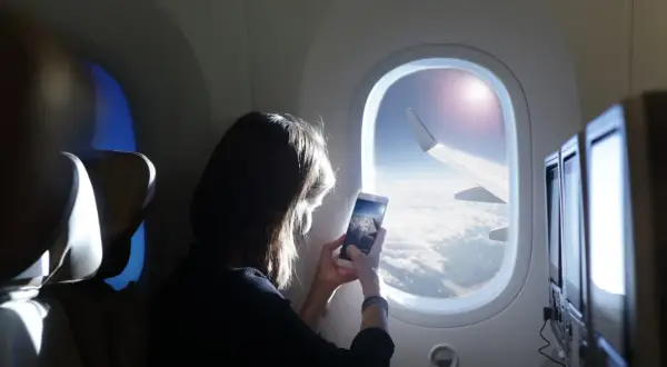 Kobieta robi zdjęcie z telefonu widoku z okna samolotu. Widok na chmury i skrzydło samolotu. Idealny moment dla tych, którzy nie boją się wysokości i chcą uwiecznić podróż.