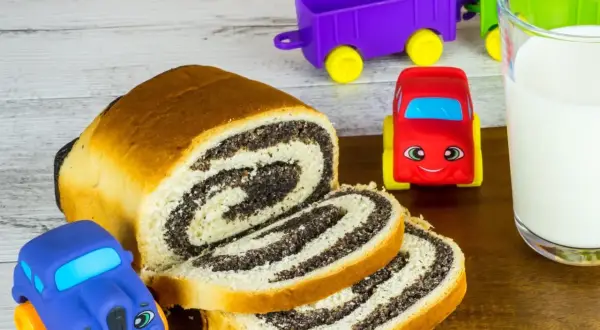 Słodki makowiec i mleko dla dzieci. Zabawki w kształcie samochodzików i wagoników zachęcają do jedzenia.