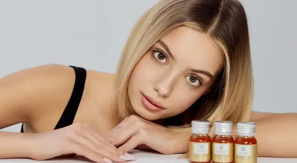 Młoda kobieta z blond włosami i delikatnym makijażem opiera głowę na rękach, obok niej stoją trzy małe buteleczki z płynnym kolagenem. Pytanie brzmi: czy kolagen można przedawkować?