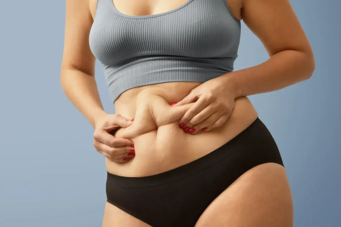 Dłonie chwytają fałdy skóry na brzuchu, ukazując sylwetkę skinny fat.