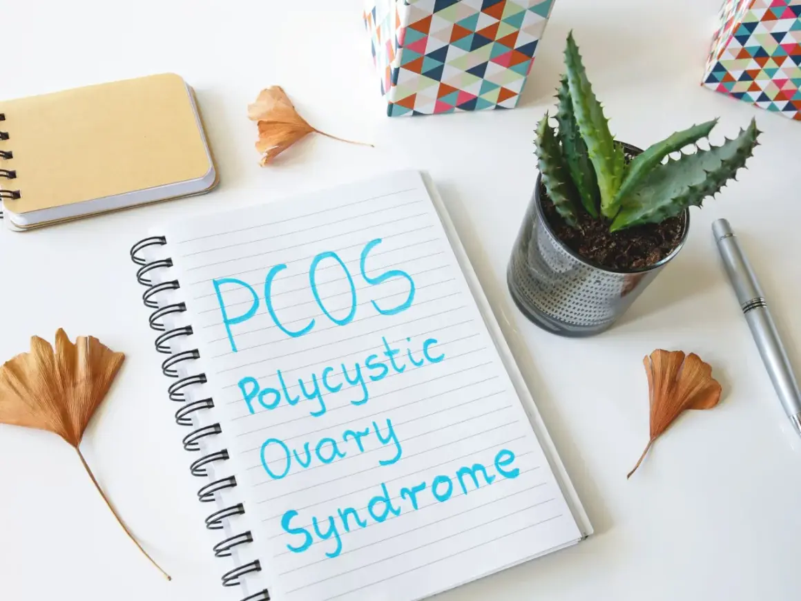 Notatnik z napisem "PCOS Polycystic Ovary Syndrome" obok sukulentów i ozdobnych pudełek. Planowanie diety PCOS.