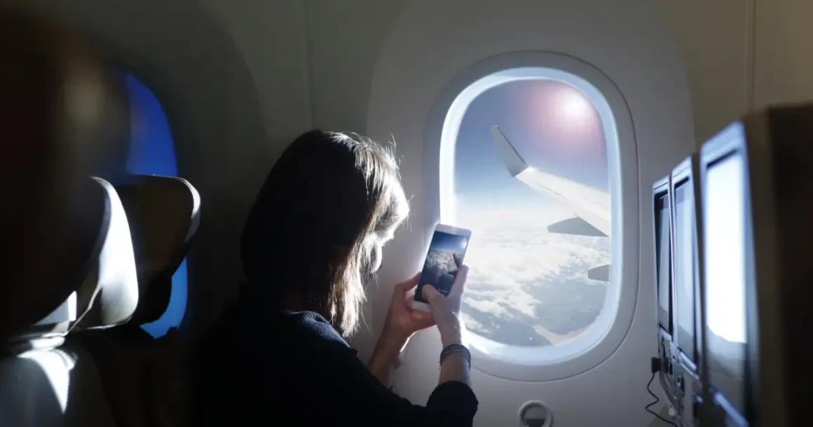 Kobieta robi zdjęcie z telefonu widoku z okna samolotu. Widok na chmury i skrzydło samolotu. Idealny moment dla tych, którzy nie boją się wysokości i chcą uwiecznić podróż.