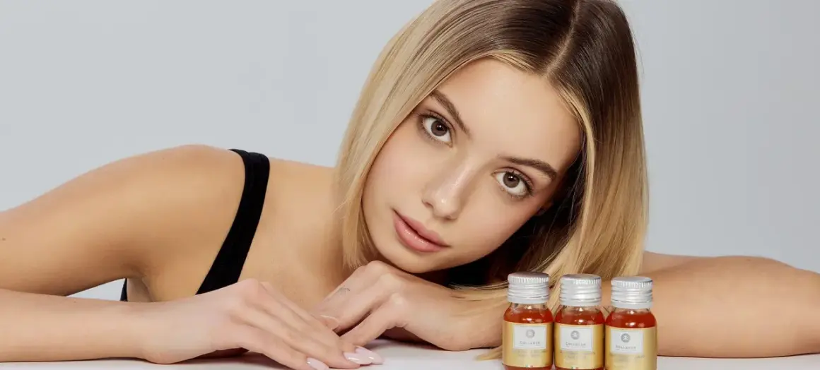 Młoda kobieta z blond włosami i delikatnym makijażem opiera głowę na rękach, obok niej stoją trzy małe buteleczki z płynnym kolagenem. Pytanie brzmi: czy kolagen można przedawkować?