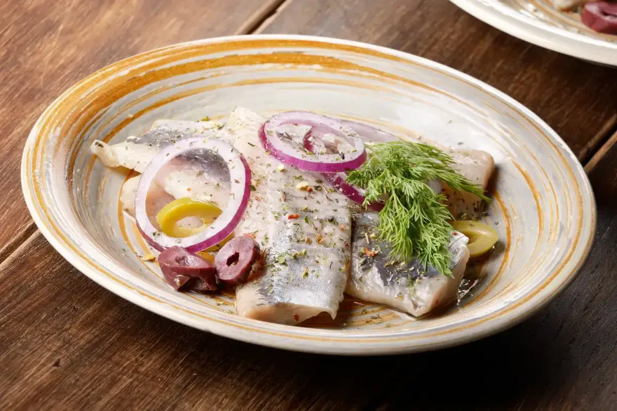 Pyszny śledź z cebulą i oliwkami, przyprawiony ziołami. Czy śledź jest zdrowy? Tak, to bogactwo kwasów omega-3!